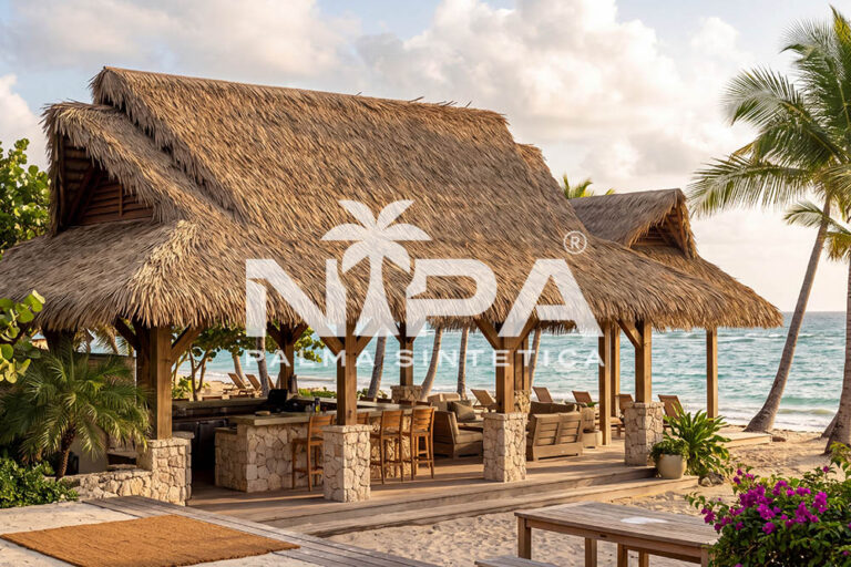 Beach restaurant with a multi-gabled synthetic palm thatch roof, timber columns on stone bases and the sea in the background