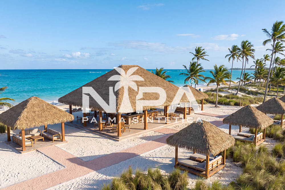 Aerial view of a large synthetic palm thatch palapa surrounded by small palapas over beach beds