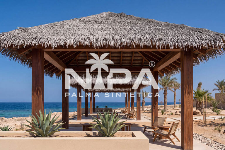 Square synthetic palm thatch palapa with dark timber posts, agaves and wooden armchairs by the sea
