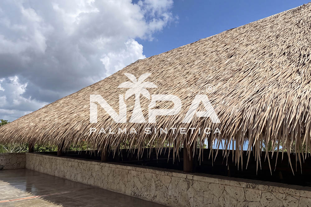Close-up of the eave line of a synthetic palm roof over a low stone wall