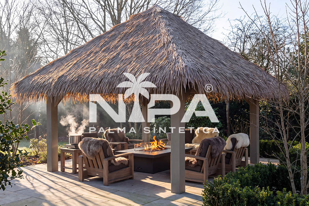 Pérgola cuadrada con cubierta de palma sintética, sillones y mesa de fuego en un jardín